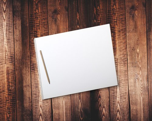 A clean reusable glass water container standing on a wooden workspace desk next to a notepad