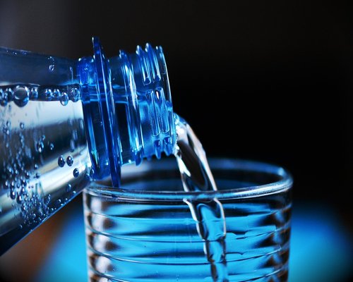A clear glass of mineral water placed prominently beside modern laptop equipment